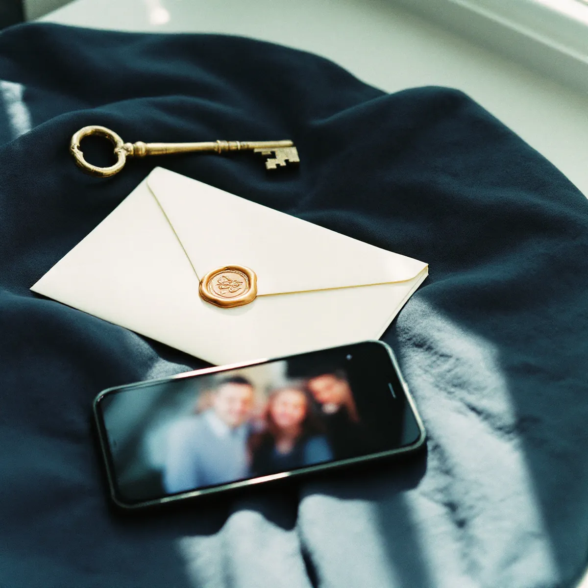 A sealed letter, a brass key and a phone resting on navy linen